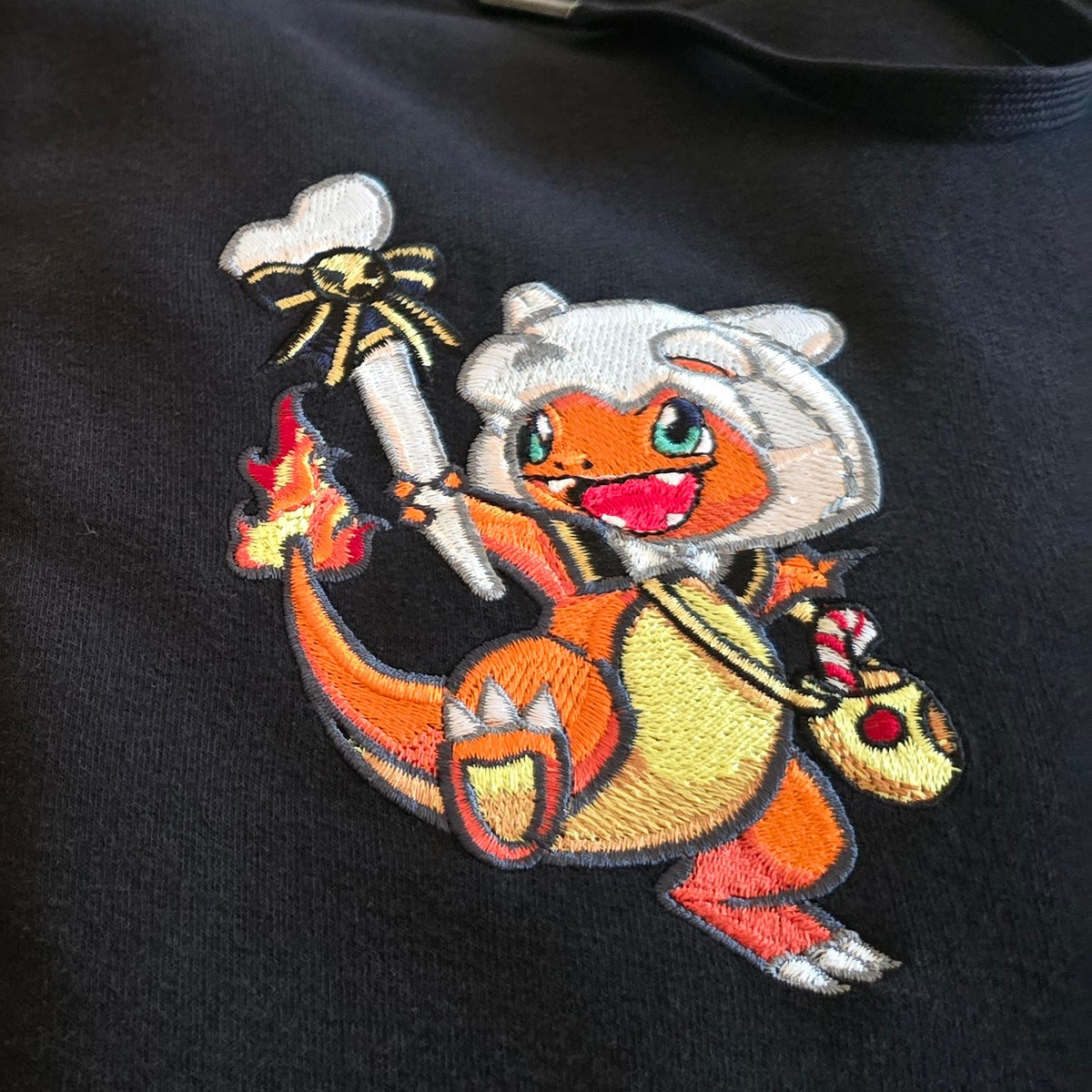 Détail de la broderie Salamèche en costume d’Osselait avec son sac de bonbons